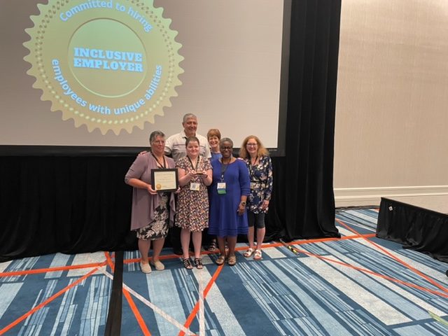 A few members of The Village at Gainesville team holding the award and certificate and standing in front of a projector